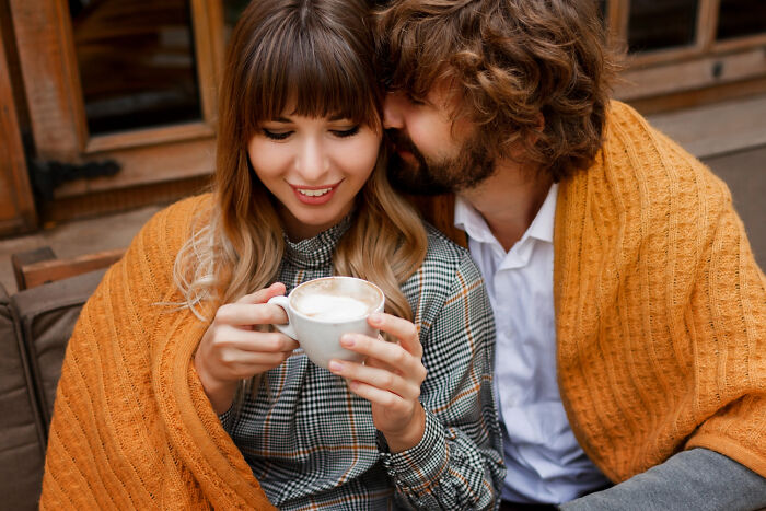 Couple wrapped in an orange blanket enjoying coffee together, illustrating dating older people stories single moments.