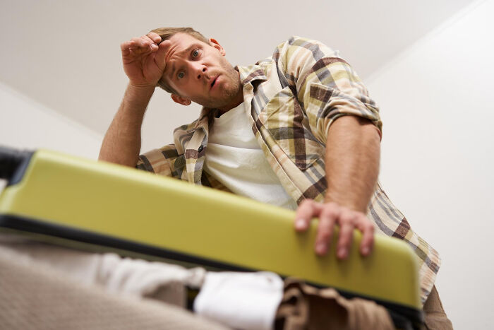 Man in casual shirt looking surprised while packing an open suitcase, relating to dating older people stories single.