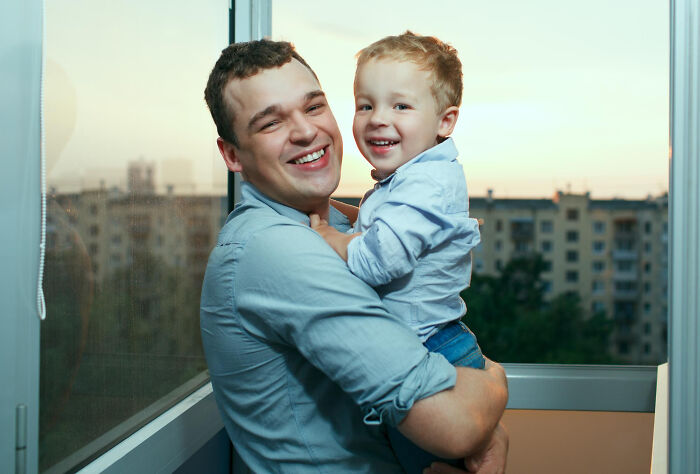 Smiling man holding young boy by window, both wearing blue shirts, representing dating older people stories single moments.