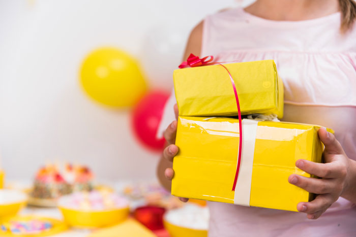 Teen holding yellow birthday gifts at a party, highlighting 13YO refusing to invite one girl from school.