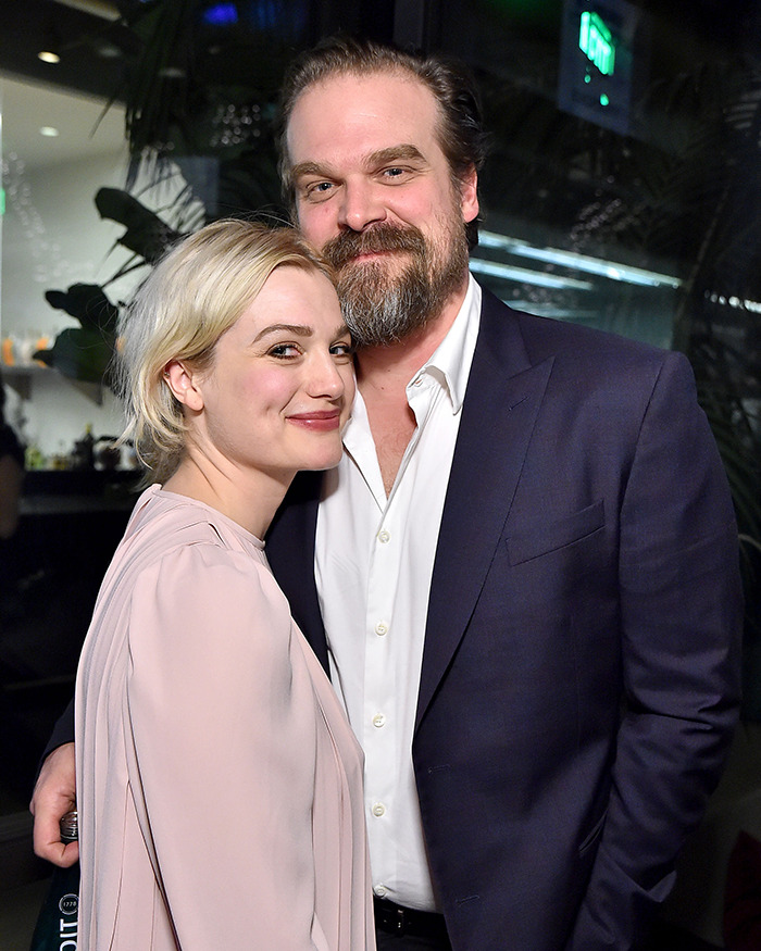 Alison Sudol smiling and posing closely with a bearded man in a dark suit jacket at an indoor event.
