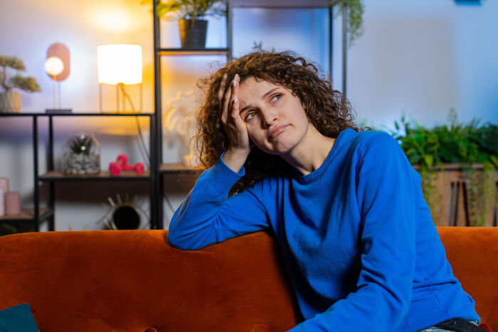 Young woman in blue sweater looking worried while sitting on a couch, reflecting on couple plans and family conflict over son.