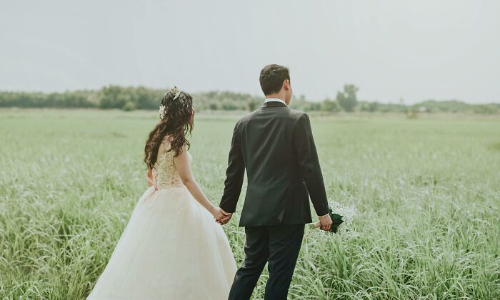 Bride and groom holding hands walking through a green field, symbolizing family and relationship challenges.