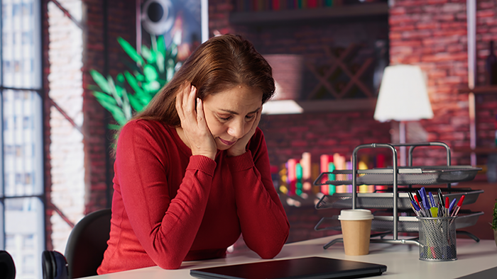 Woman in red sweater looking stressed and regretful while sitting at desk, reflecting on neglecting siblings and wanting to reconnect.