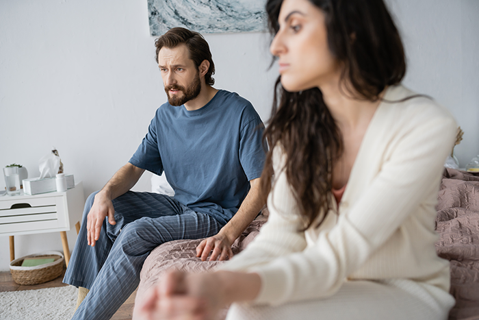 A couple sits apart on a bed, showing tension after a confrontation about Thanksgiving food hogging by MIL. A couple sits apart on a bed, showing tension after a confrontation about Thanksgiving food hogging by MIL.