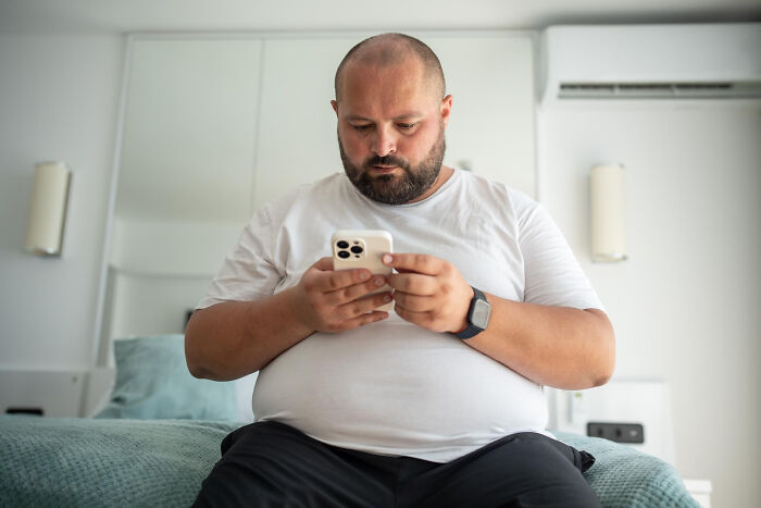Man in a white shirt using a smartphone on a bed, illustrating Dr. Google versus a real doctor scenario.