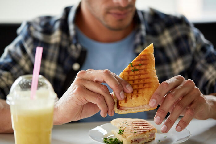 Man holding a grilled sandwich with a smoothie nearby, illustrating a casual moment of Dr Google versus real doctor advice.