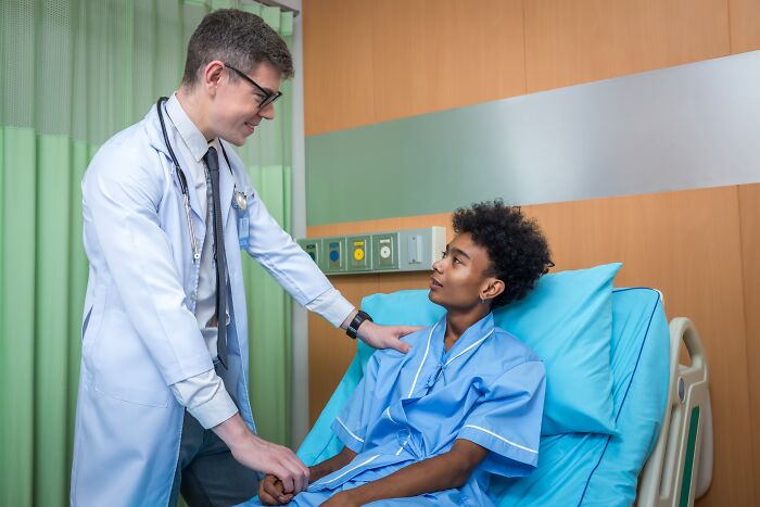 Doctor comforting patient in hospital bed, capturing eerie moments patients said that still haunt doctors today.