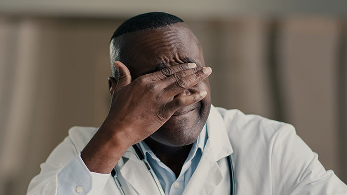Doctor in a white coat covering his face with his hand, showing stress and regret over a medical mistake.