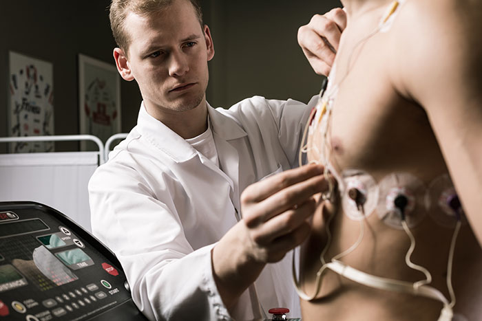 Doctor attaching electrodes to a patient’s chest during a cardiac test in a clinical setting, highlighting medical care by surgeons.