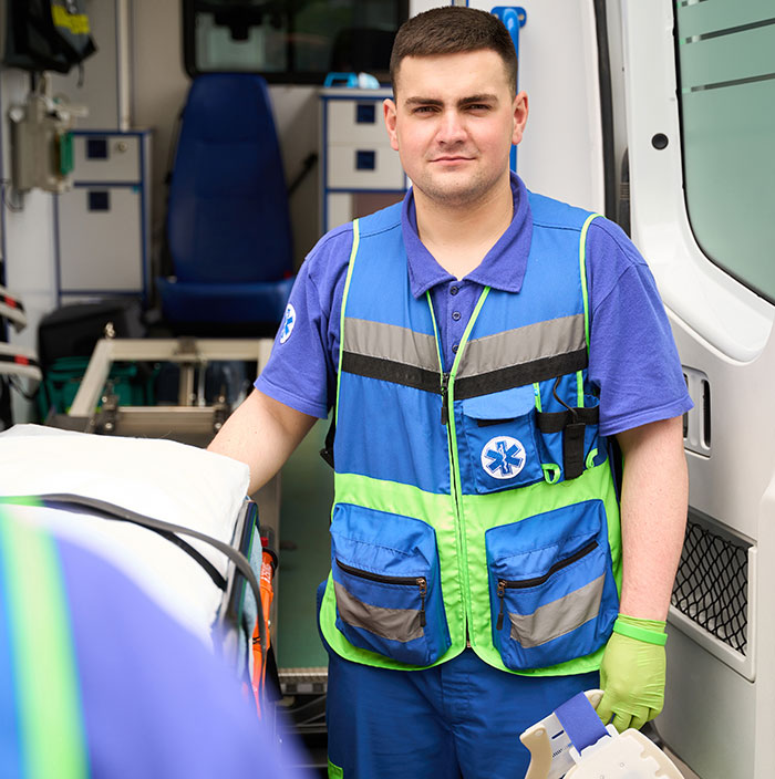 Paramedic wearing medical vest and gloves standing by ambulance stretcher representing surgeons and doctors recalling mistakes.