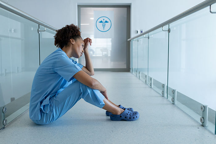 Female surgeon in scrubs sitting on hospital floor looking stressed, reflecting on medical mistakes and challenges.