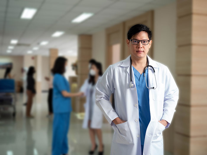 Surgeon in white coat with stethoscope in hospital corridor with medical staff, illustrating doctors recalling their worst mistakes.