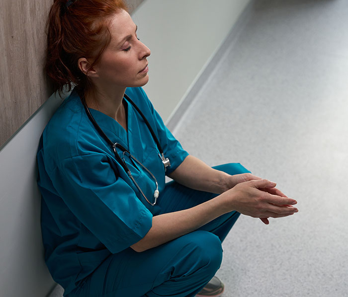 Female surgeon in scrubs sitting on floor looking distressed, reflecting on worst mistakes in medical practice.