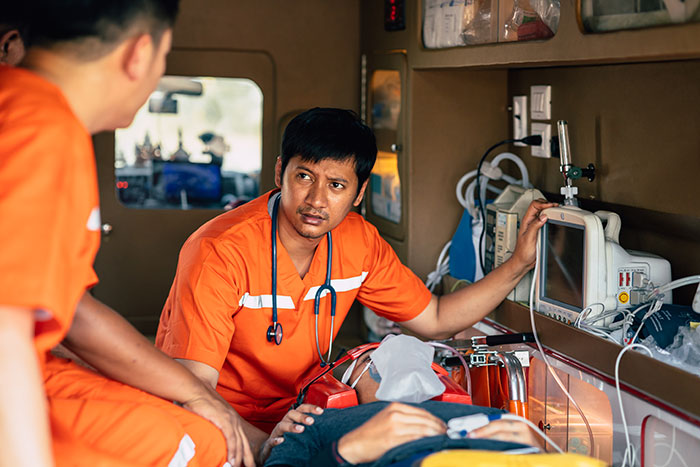 Two doctors in orange uniforms attending to a patient inside an ambulance monitoring vital signs and medical devices.