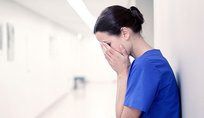 Female surgeon in blue scrubs covering her face in a hospital hallway, reflecting on medical mistakes and professional challenges