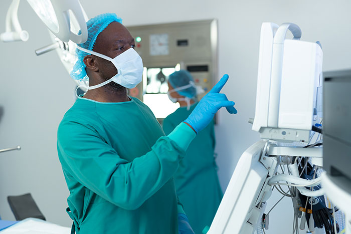 Surgeon in scrubs and mask reviewing medical monitor during surgery, highlighting doctors recalling mistakes in clinical settings.