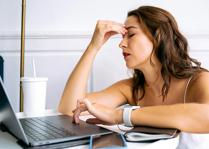 Woman stressed working on laptop, illustrating MIL scheduling important family events on woman&rsquo;s work days conflict
