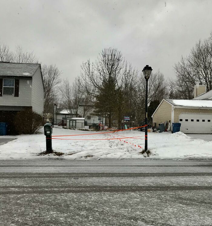 Snowy suburban driveway blocked with orange string between mailbox and lamppost as petty revenge example.