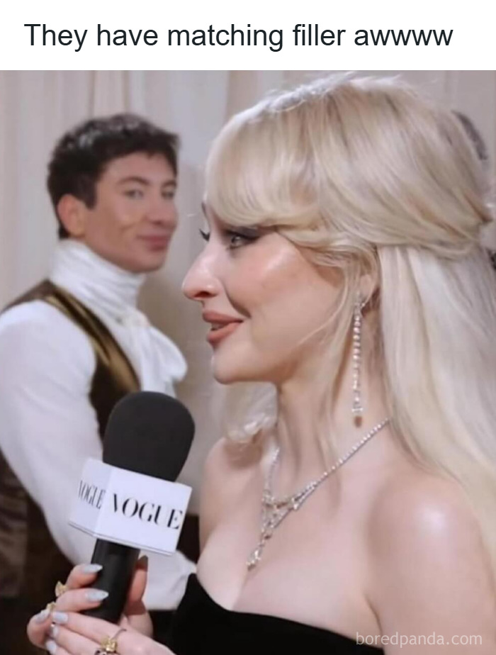 Woman with glamorous makeup and jewelry being interviewed, with a man in makeup and fashion in the background, diva life vibe.