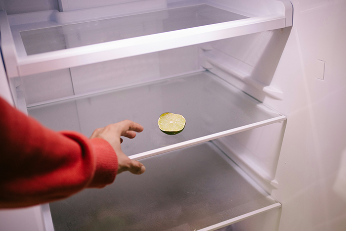 Hand reaching into nearly empty fridge with a single lime, illustrating parenting challenges and kids buying their own food.