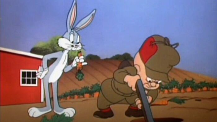 Bugs Bunny holding a carrot behind Elmer Fudd who is aiming a gun in a cartoon scene explaining word etymology.