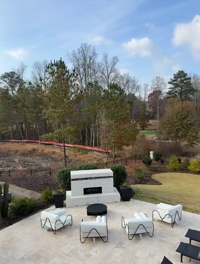 Outdoor patio with white chairs and fireplace overlooking area where trees were bulldozed sparking tree law debate.