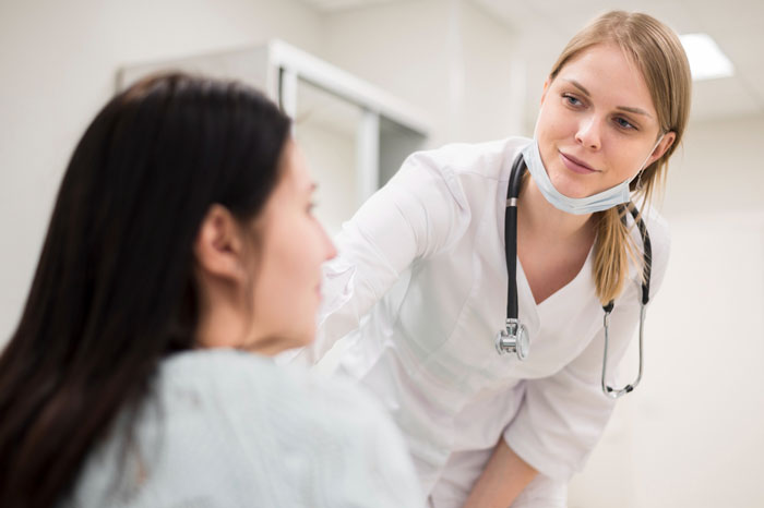 Female ER staff wearing a stethoscope attentively speaking to a patient in a hospital setting demonstrating care and authority.