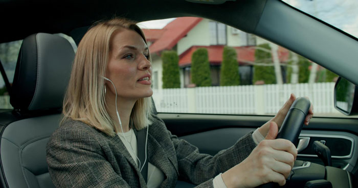 Woman with headset driving a car, appearing frustrated as she tries to impose her rules on ER staff.