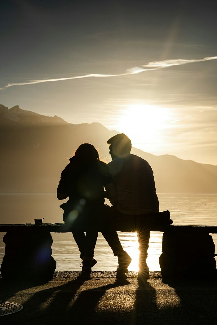 Silhouettes of a couple sitting by the lake at sunset, reflecting on love and friendship affected by broken trust.