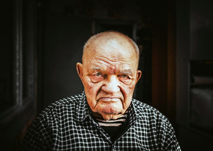 Elderly man with serious expression in a dark room, illustrating stories of families where the golden child changes over time.