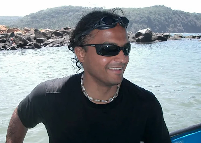 Man wearing sunglasses and a shell necklace smiling on a boat near rocky shore, related to toxic tech CEO story.