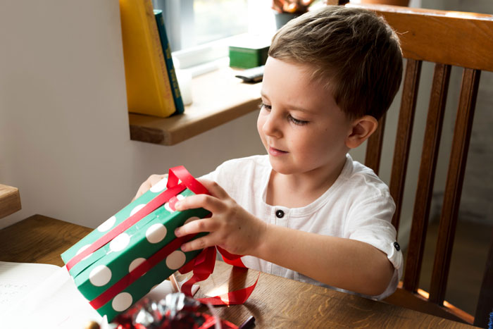 Young boy opening a gift box with AirPods inside while mom worries about traceable device concerns.