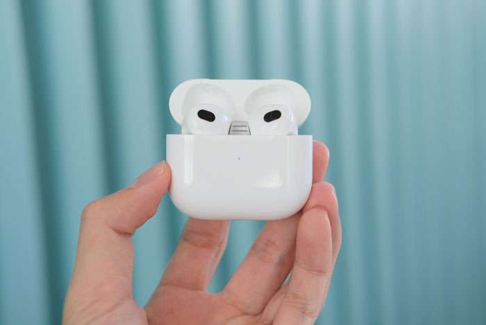 Hand holding brand-new AirPods in charging case highlighting traceable wireless earbuds technology.