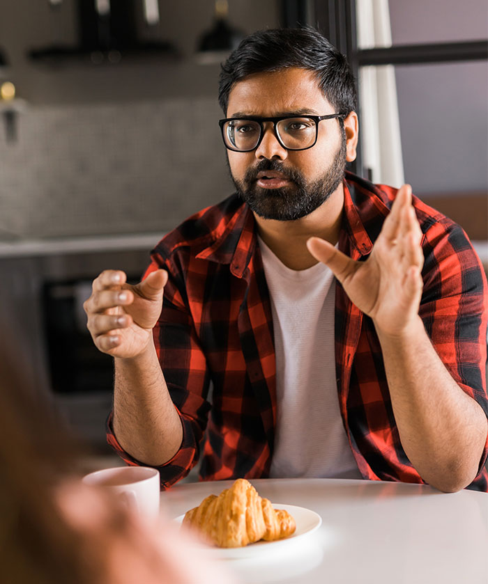 Man in red plaid shirt and glasses gesturing while talking during a tense discussion about toxic ex and constant threats