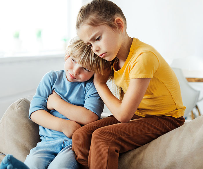 Young girl comforts brother on couch, illustrating woman dealing with toxic ex and his constant threats concept.