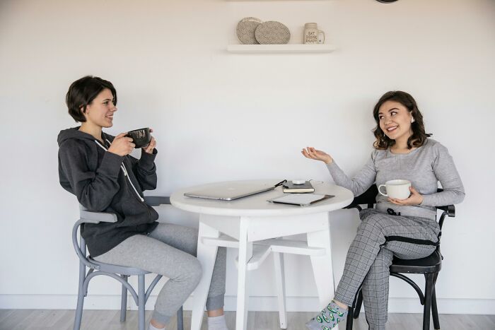 Two women having coffee and chatting at a small table while discussing annoying life choices in a casual setting