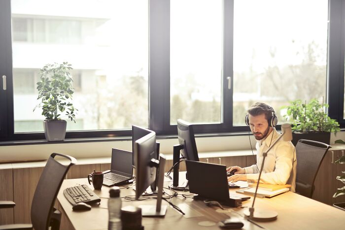 Man wearing headset working on computer in bright office, illustrating annoying life choices in a 50-50 poll setting.