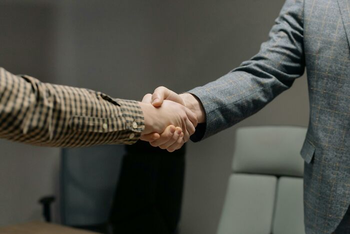 Two people shaking hands in a formal setting, illustrating the concept of annoying life choices in a 50-50 poll.