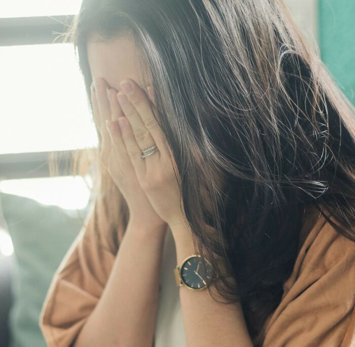 Woman covering her face, wearing an engagement ring, expressing distress in a moment of uniquely awkward wedding troubles.