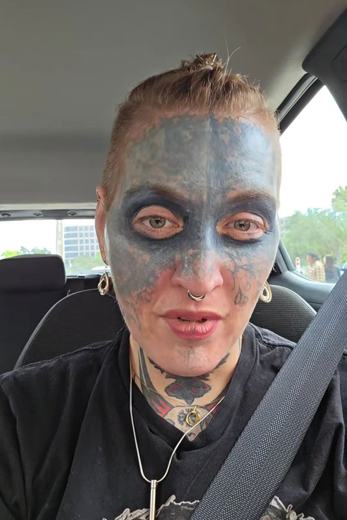 Woman with prominent face tattoo speaking about mental health advocacy while wearing a seatbelt in a car.