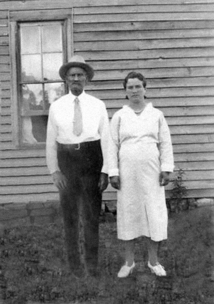 Black and white photo of a man and woman outside a wooden house, illustrating true facts that make others question if they’re real.