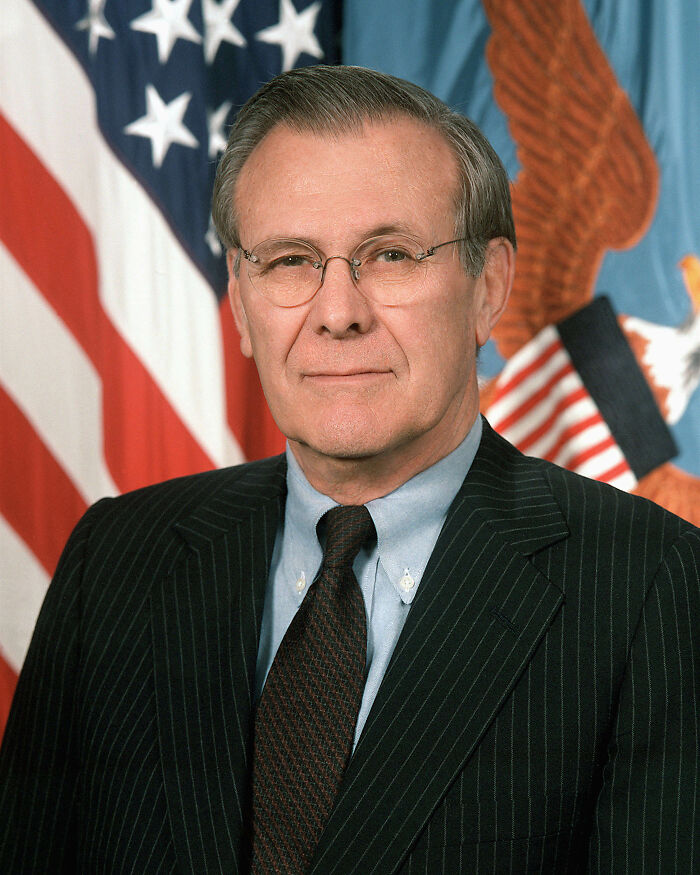 Older man in a pinstripe suit and glasses posing in front of American flag, illustrating favorite true facts that seem unreal.