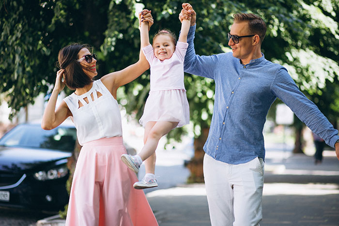 Family enjoying time outdoors, husband and wife lifting daughter, reflecting husband ban daughter nanny Spanish lessons theme.