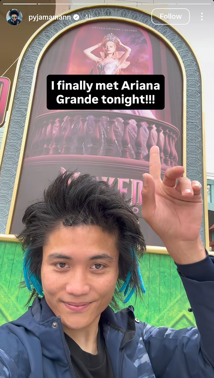 Young man with blue-tipped hair posing in front of promotional poster referencing Ariana Grande at a premiere event.