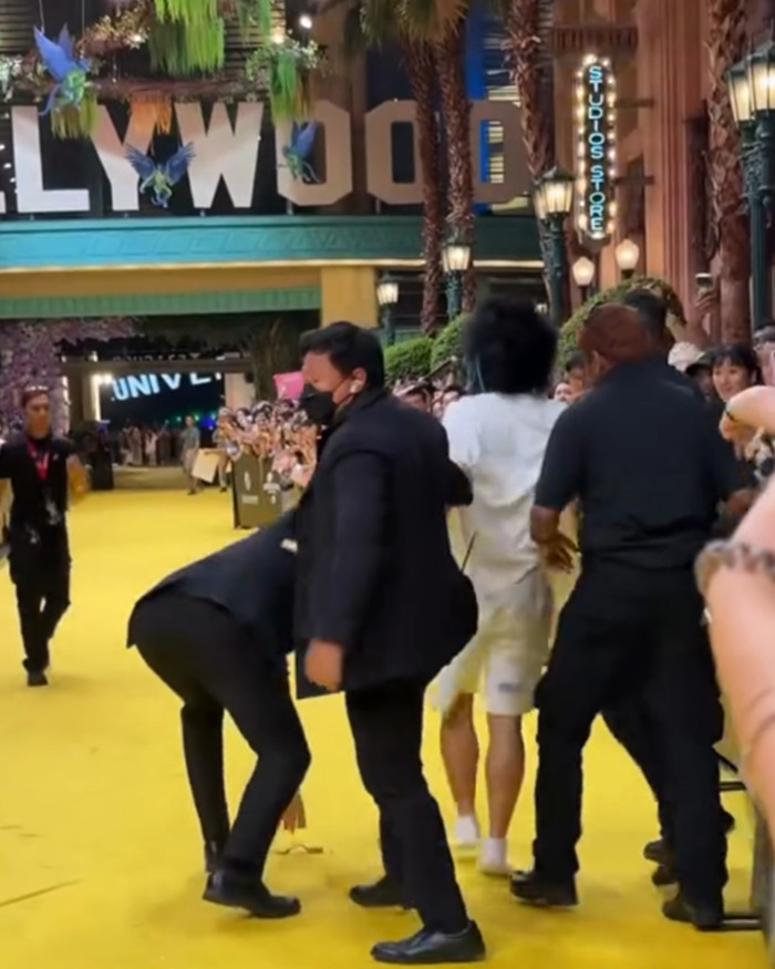 Security personnel restraining a fan who attacked Ariana Grande at a premiere as crowd looks on and records the event.