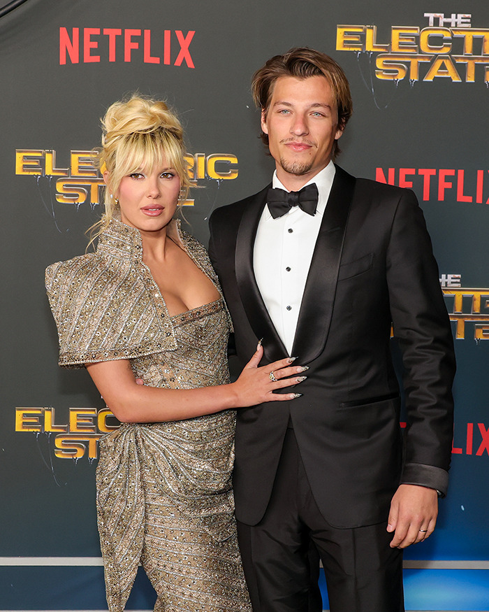 Millie Bobby Brown and Jake Bongiovi posing on the red carpet at a formal Netflix event.