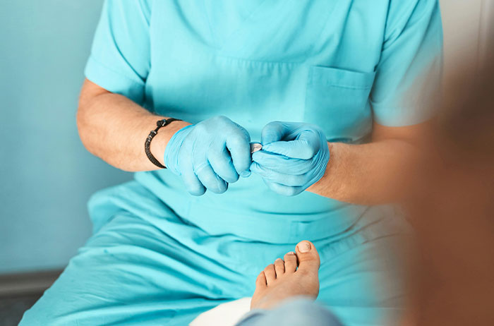 Medical professional wearing blue gloves trimming toenails of a patient, depicting unexpected life stories ending.