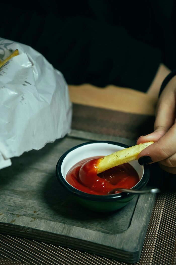 Hand dipping French fry into ketchup, capturing a relatable moment in parents raising monsters with messy eating habits.