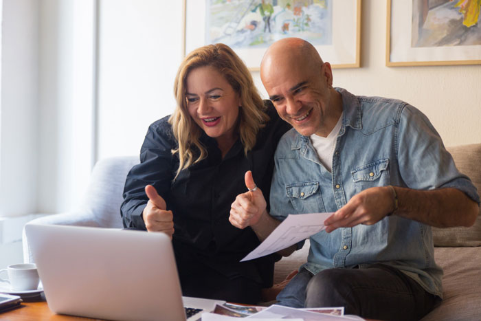 Man and woman smiling and giving thumbs up while discussing documents on a laptop about charging daughter $15K for raising her Man and woman smiling and giving thumbs up while discussing documents on a laptop about charging daughter $15K for raising her